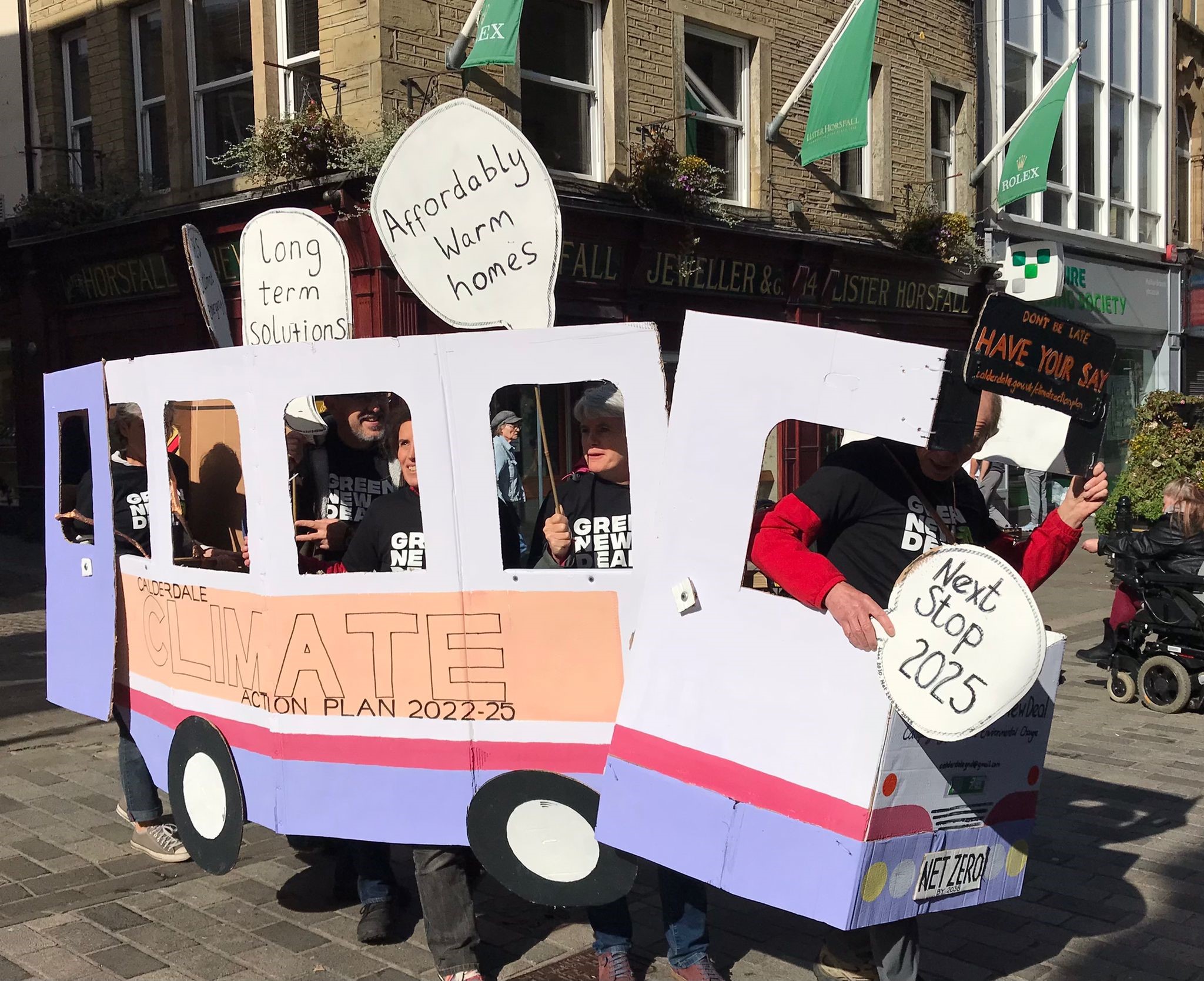 A group walking along carrying a bus made of card and climate slogans
